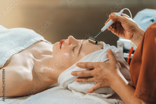 Beautiful young women lie on spa bed while having facial massage from professional doctor. Attractive female with beautiful skin surrounded by electric facial machine. Tranquility.
