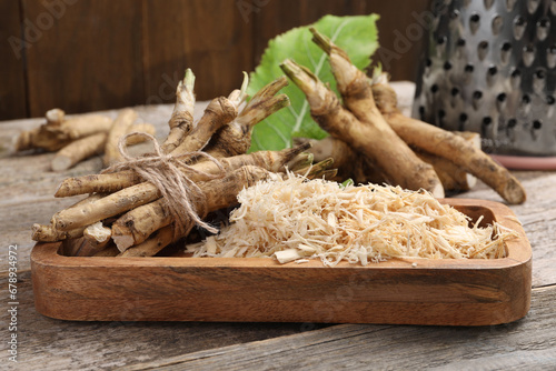 Grated horseradish and roots on wooden table, closeup