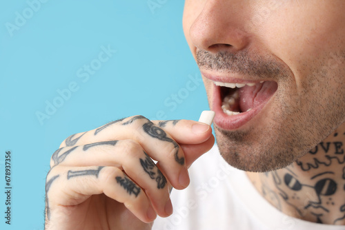 Young tattooed man with chewing gum on blue background, closeup