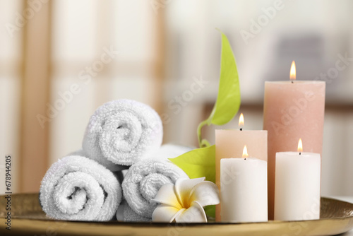 Spa composition. Burning candles, plumeria flower, green leaves and towels on tray