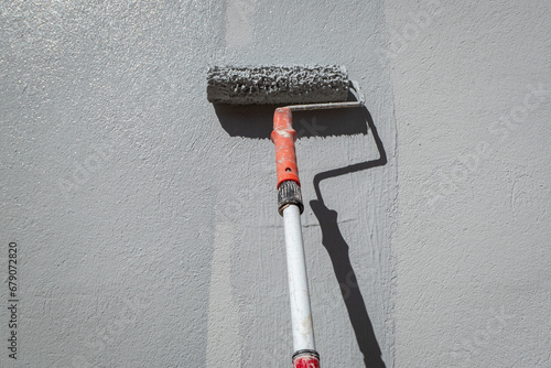 O pintor com o seu rolo na vara de pintor a pintar a parede