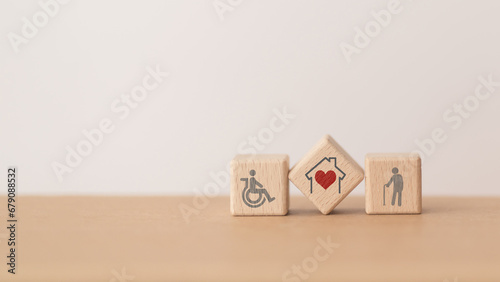 house with red heart inside wooden cube block and elderly and disability person icon, including copy space, for home or nursing care for aging people concept