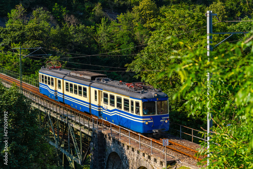 Historic electric train on famous steel bridge in Intragna in Centovalli valley. Narrow gauge railway line from Locarno to Domodossola in Italy in the Swiss Alps. Popular tourist train attraction.