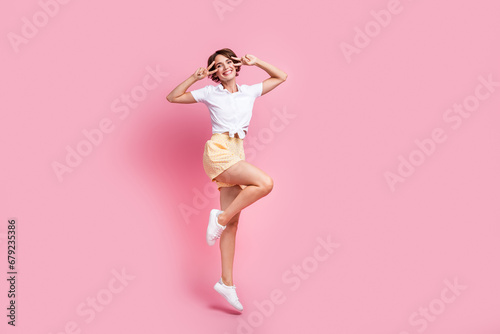 Full length photo of jumping trampoline funky active lady wearing spring season apparel cover eyes v sign isolated on pink color background