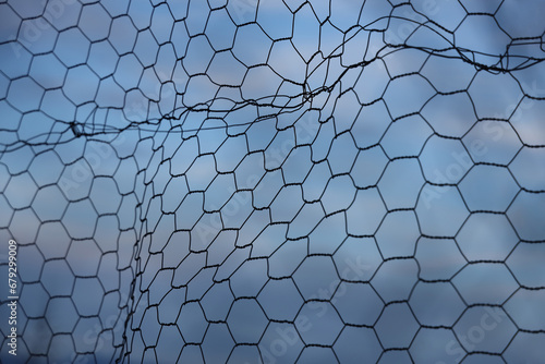Chain-link fence fragment. fine twisted wire isolated on blue cloudy sky background. Secured territory, protected area fencing.