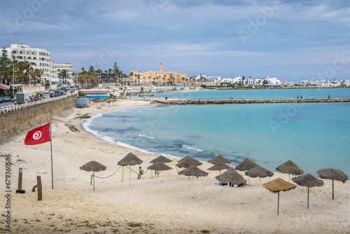 The beach and Mediterranean sea coastline at resort town of Monastir, Tunisia, with the long pier, Tunisian flag, umbrellas, waterfront, and Raban (castle) at old town at the background.