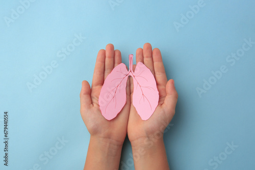 Child holding paper human lungs on light blue background, top view