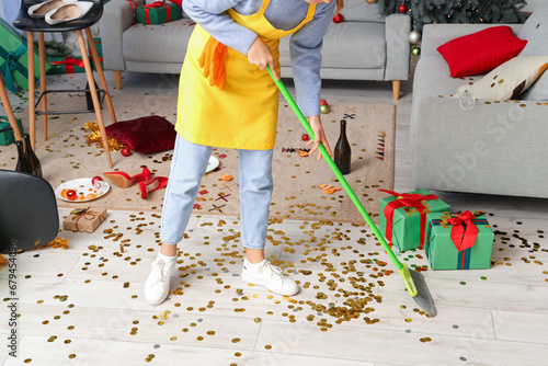 Female janitor sweeping floor in messy living room after New Year party
