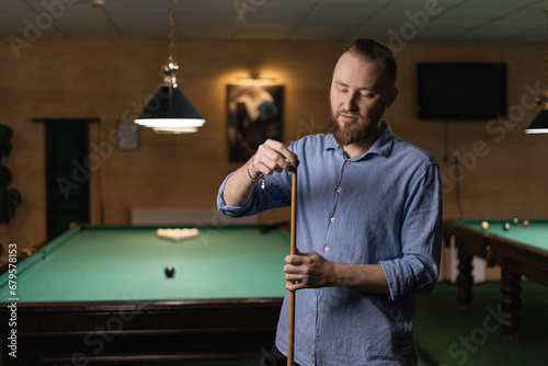 Male snooker player prepares to play billiards by rubbing his cue with chalk to prevent it from slipping.