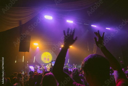 crowd of people dancing at concert, silhouette of hands, purple light on stage at concert
