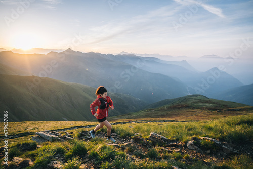 Female trail runner ascending alpine trail in the mountains at sunrise
