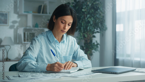Business woman is writing on a notepad with a pen and using a laptop computer. Doing homework. Concept of lifestyle and work at home. Creative paper plan, idea or reminder for business goals