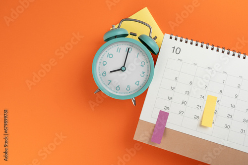close up of calendar and alarm clock on the orange table background, planning for business meeting or travel planning concept