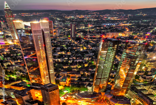 Die Skyline von Frankfurt am Main mit Hochhäusern und Straßenzügen der Innenstadt aus der Luft in der Dämmerung mit künstlicher Strassenbeleuchtung