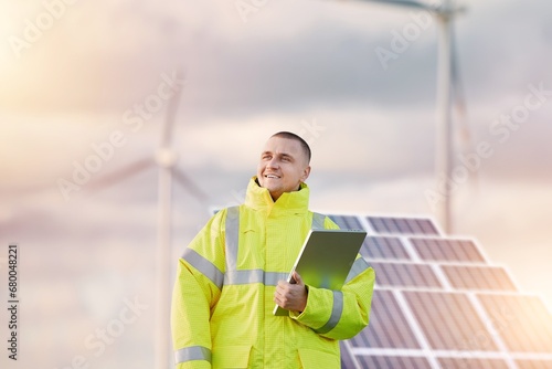 Wind turbine and solar panels engineer. Male engineer maintains and controls wind turbine energy generation on the background of windmills. Concept of sustainable future and green electrical enerygy.