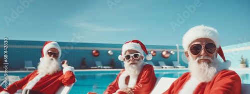 Three Santa Clauses with white beards and traditional costumes relaxing near the swimming pool. Christmas vacation concept.