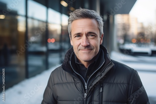 Portrait of a grinning man in his 50s sporting a quilted insulated jacket against a sophisticated corporate office background. AI Generation