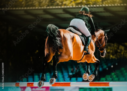 A beautiful bay horse with a rider in the saddle jumps over a high barrier against the background of the stadium at equestrian show jumping competitions, rear view. Equestrian sports and horse riding.