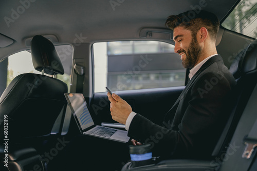 Handsome businessman in suit using personal computer and using mobile phone in taxi