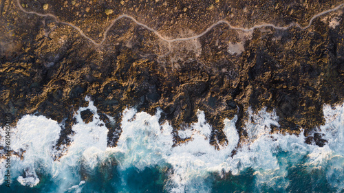 Drone view of Tenerife south coast with Atlantic ocean and strong swell beating against the walls of a rocky cliff, blue rough sea with big waves with foam crashing against the rocks