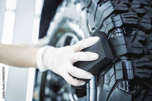 Professional car service worker polishing car tires with black sponge