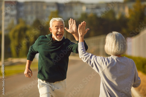 Good job. Well done. Two happy old people finish jogging and have fun. Cheerful excited male athlete in sportswear high fives female partner after outdoor spring summer running workout. Sport concept