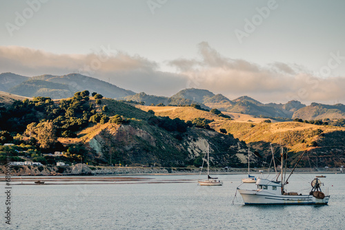The picturesque scene unfolds as rolling hills meet the tranquil sea, adorned with boats moored along the coastline
