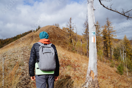 Back view of man with backpack on mountainside, hiking in the forest, hiking route in the mountains.
