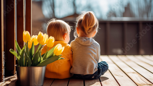 First love, rear view, children sitting next to each other on a veranda decorated with tulips, a boy and a girl. First date. Children's friendship. Spring at the dacha