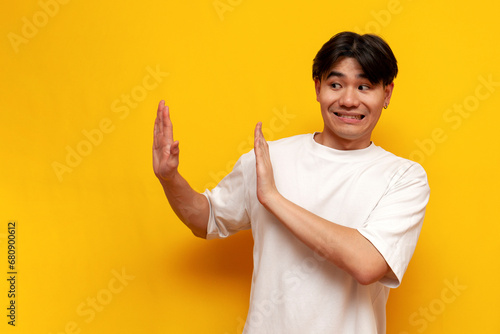young asian guy in white t-shirt refuses and avoids on yellow isolated background, korean man refuses