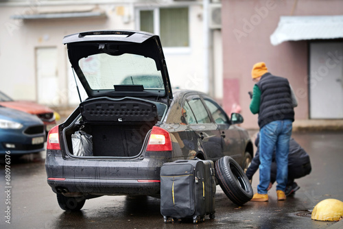 Man replacing flat tire on taxi car. Driver replace tire after puncture. Traffic accident, tire puncture. Taxi car with open trunk, clients suitcases near car with damaged wheel