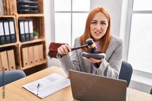 Young business woman using gavel clueless and confused expression. doubt concept.