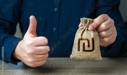 The man approves the deal or loan. Thumbs up and israeli shekel money bag. Agreement to be hired for a job at the offered salary. Financial grants and investments. Profit-generating deposits savings.