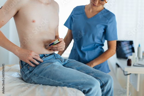 Diabetologist doctor teaching a teenage patient how to inject insulin into his abdomen, using insulin pen. Endocrinologist injecting medicine into boy's abdomen.