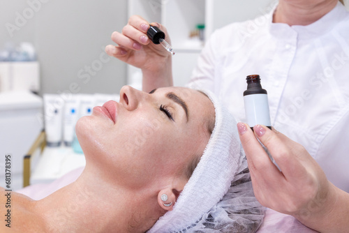 Close up of professional cosmetologist applies moisturizing serum to client woman's face. Concept of skin care and cosmetology