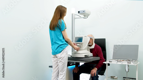 An elderly man undergoes an eye examination in a modern clinic. An expert checks vision using diagnostic ophthalmological equipment.