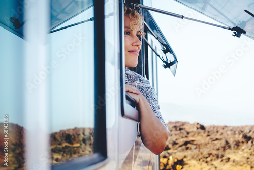 Nice adult woman smile and enjoy freedom at the natural campsite admiring outdoors outside the window of her camper car. Concept of summer tourist travel vacation and free female independence people