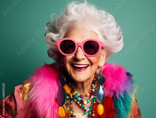 Funky grandmother laughing happily with fashionable clothes portrait, white hair and wearing trendy glasses a studio photo against neon background. Youthful grandmother with extravagant style