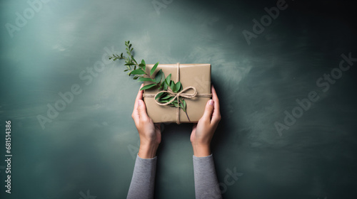 ユーカリを後ろに飾って、植物を使ったナチュラルなラッピングしたプレゼントを手包んでいるアップの写真、背景グレー