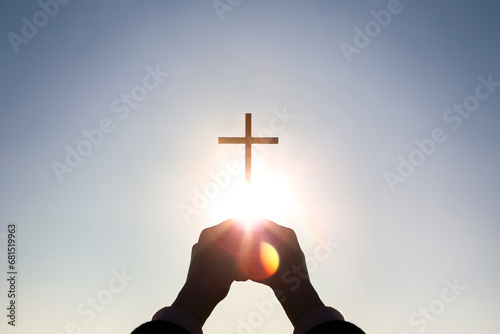 Brightly shining sunlight and silhouette of Christian hands holding high the cross of Jesus Christ symbolizing death and resurrection 