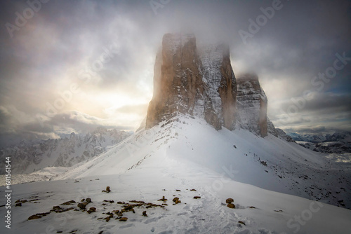 Montagnes en hiver dans une vallée brumeuse dans la neige dans le massif des Dolomites en Italie. Tre Cime di Lavaredo enneigées avec un ciel nuageux mais au travers duquel la lumière arrive à percer 