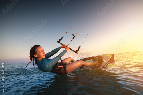 Girl kitesurfing in a sexy hydrosuit with a kite in the sky on board in the blue sea, riding on the water waves. Recreational activities, water sports, activities