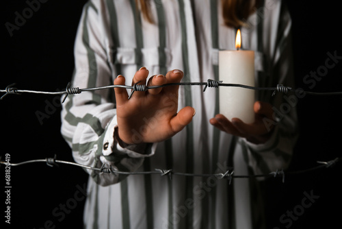 Jewish female prisoner with burning candle behind barbed wire on dark background, closeup. International Holocaust Remembrance Day
