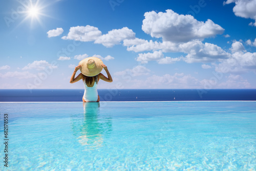 Summer holiday concept with a woman with sunhat sitting at the endge of a big infinity pool