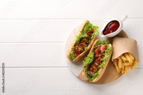 Tasty hot dogs with chili, lettuce, ketchup and French fries on white wooden table, top view. Space for text