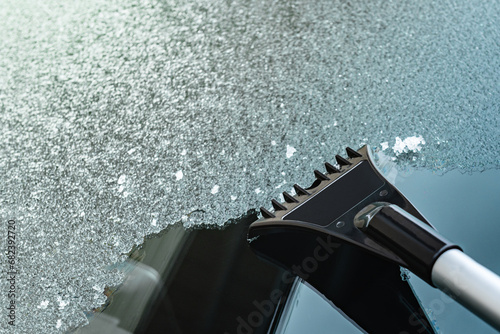 Cleaning of icy window on car with ice scraper on winter frosty morning.