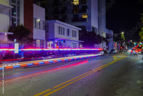 Captivating night scene of Miami Beach cityscape illuminated by mesmerizing defocused light trails left behind by cars navigating Collins Avenue.