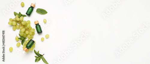 Bottles of essential oil, ripe grapes and mint leaves on white background with space for text