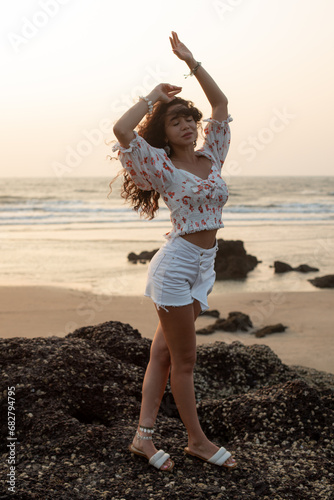 Portrait of young Asian woman standing on stones near beach, raising hands with closed eyes, enjoying holiday. Beauty.