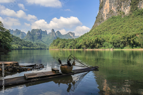 Landscape of karsten mountain along the Li River in Guilin with a bamboo raft and two comorants perching on fish basket